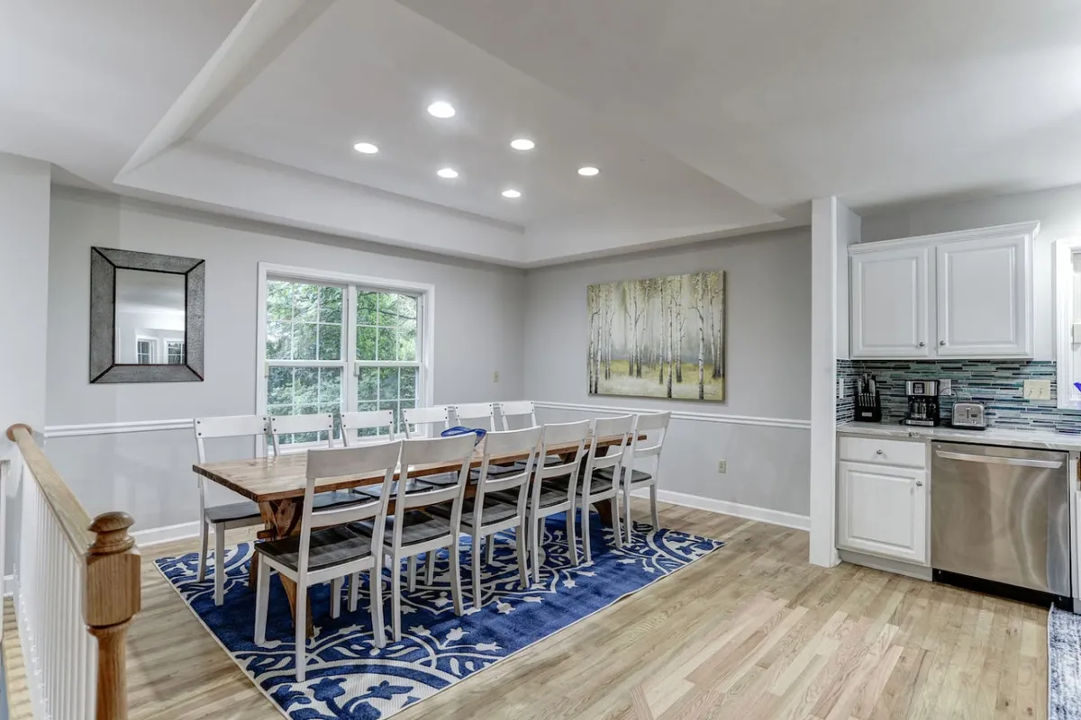 A warm dining room scene where a large table is the centerpiece, surrounded by comfortable seating and accented by artwork. The adjoining kitchen is visible, seamlessly connecting meal prep and dining experiences.
