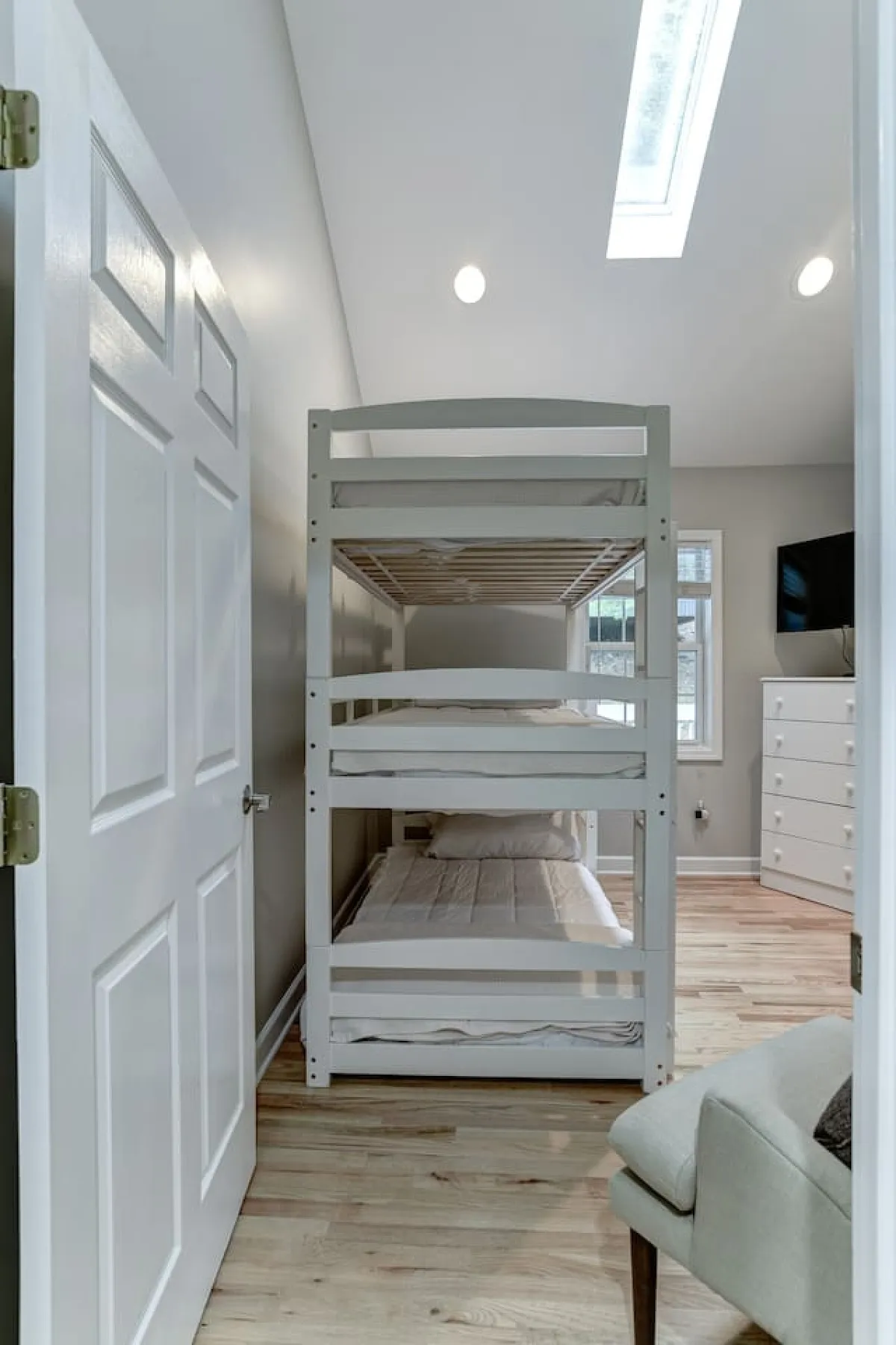 A comfortable bedroom with a bunk bed, a dresser, a window bringing in morning light, and a cozy seating area. The room is versatile and welcoming for kids or singles, providing flexible sleeping arrangements.