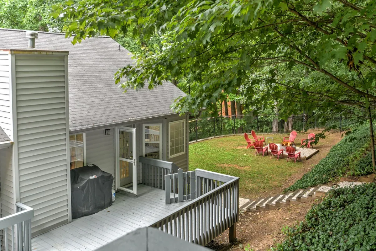 The image displays a spacious wooden deck surrounded by lush greenery, featuring Adirondack chairs, a grill, and a fire pit. The inviting outdoor space suggests an ideal setting for relaxing after a day of adventures or for gathering with family and friends to share stories.