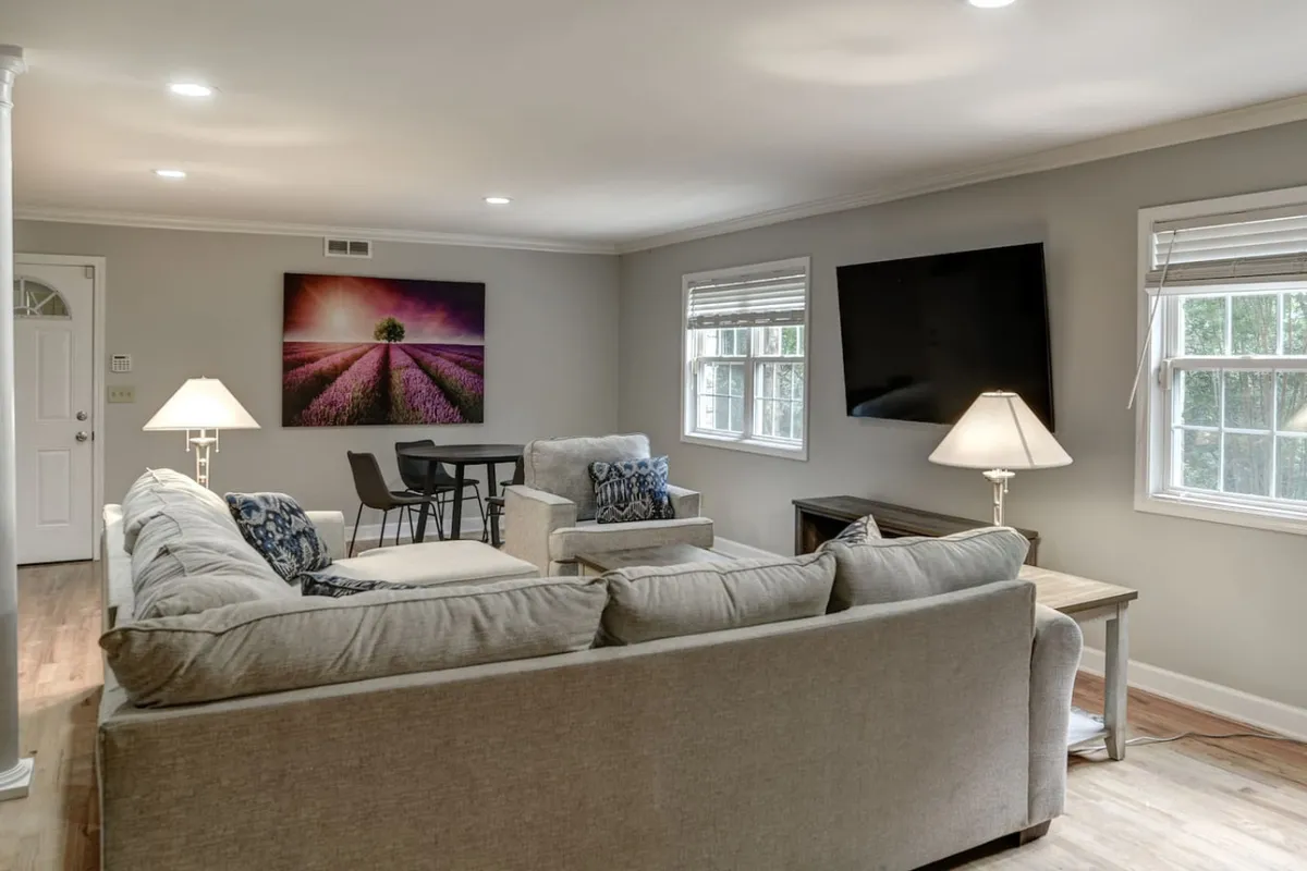 A spacious, comfortable living area featuring a large sectional sofa, wall artwork, television, and a dining table with chairs. The open layout allows for fluid movement between lounging, dining, and entertainment spaces.