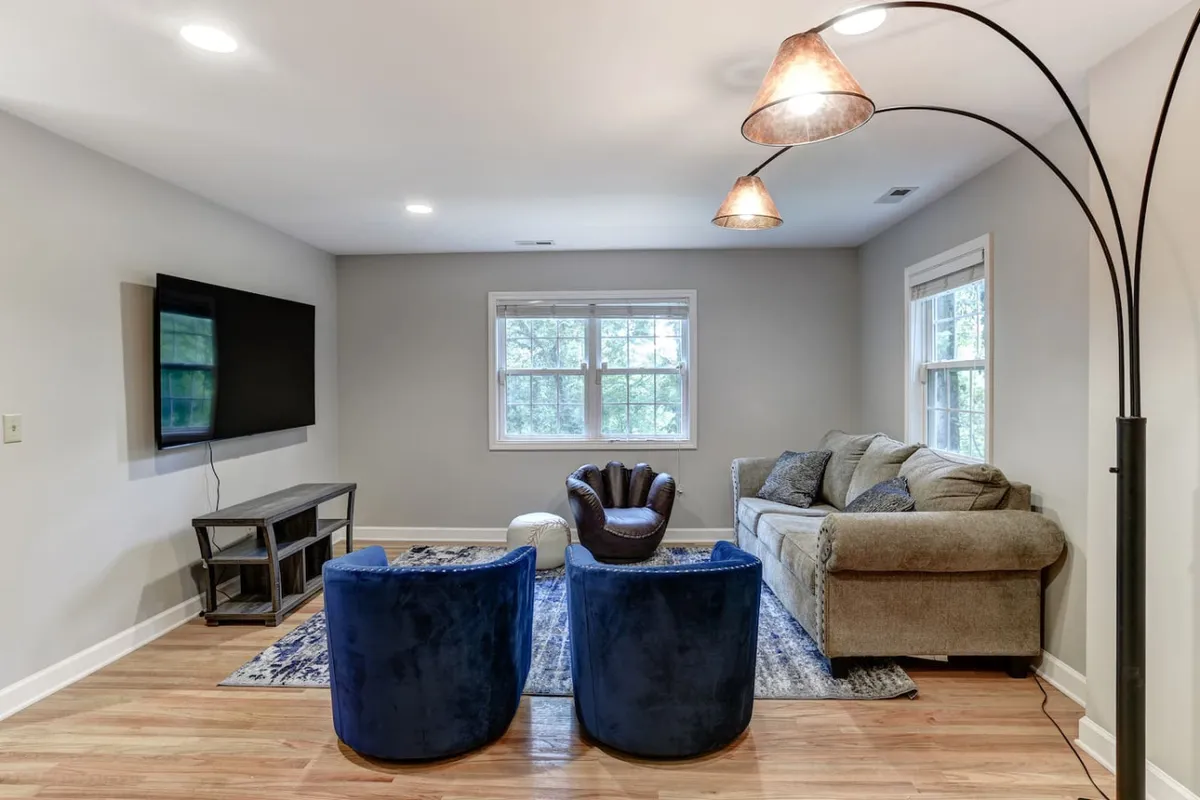A cozy living area featuring a sofa, blue accent chairs, a television, and a soft rug—arranged for conversation, watching movies, or gathering for games. The space is comfortable and inviting, ideal for group relaxation and entertainment.