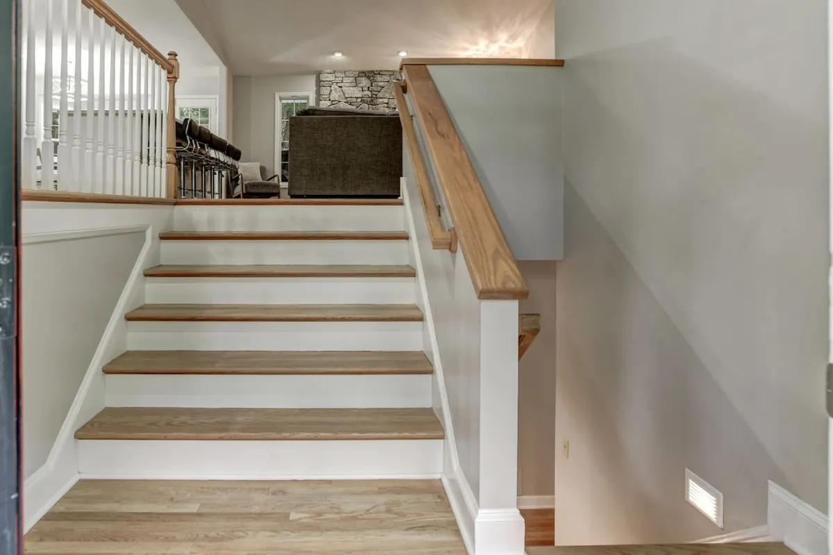 This image shows a central staircase with an inviting living area visible in the background, accented by stylish railings and light fixtures. The scene captures a sense of movement and gathering, and suggests entry into the heart of the home where group activities and socializing naturally happen.