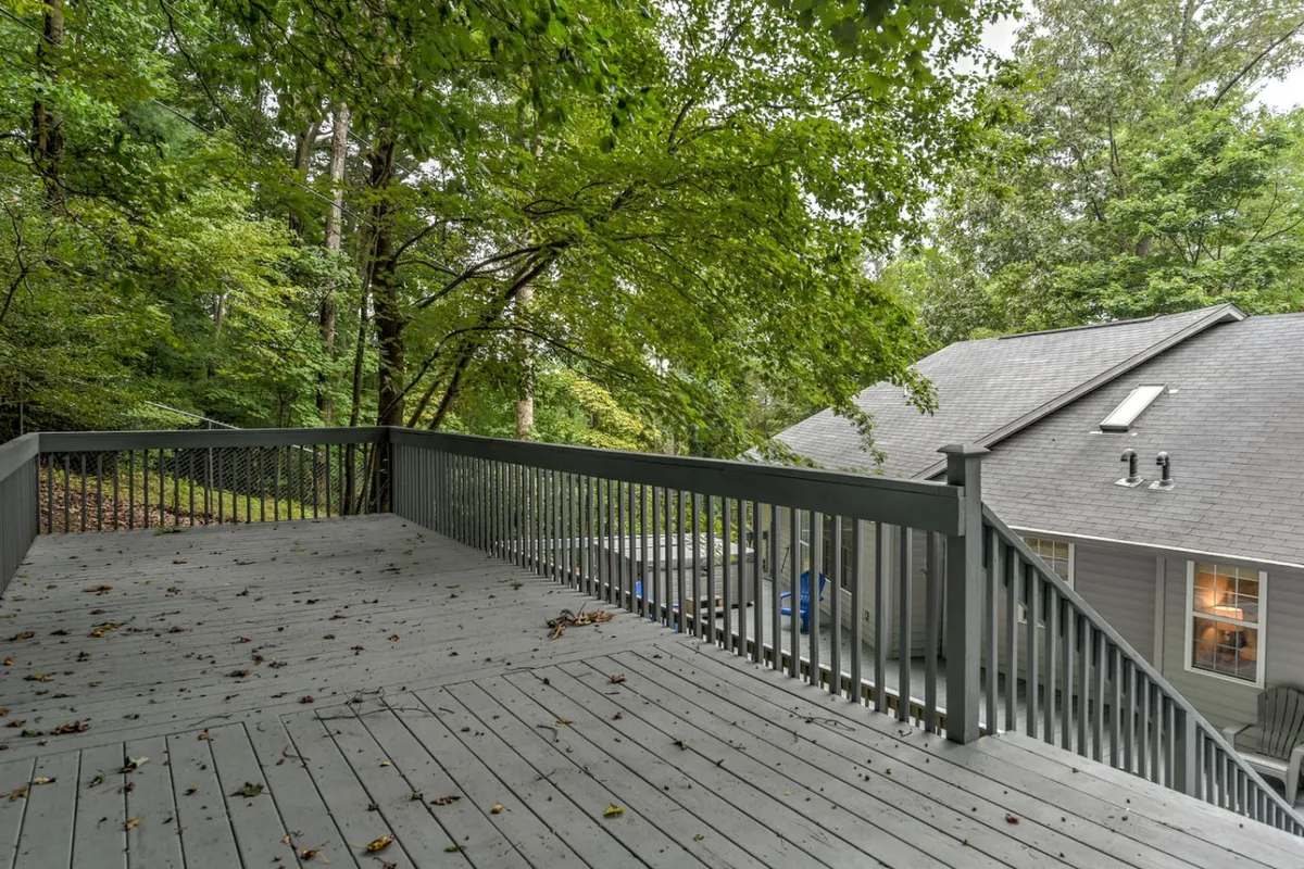 This exterior shot highlights the home’s deck railing with surrounding mature trees, offering glimpses of the house’s exterior. The peaceful setting emphasizes privacy and the allure of the natural surroundings, setting the stage for outdoor gatherings or quiet moments.