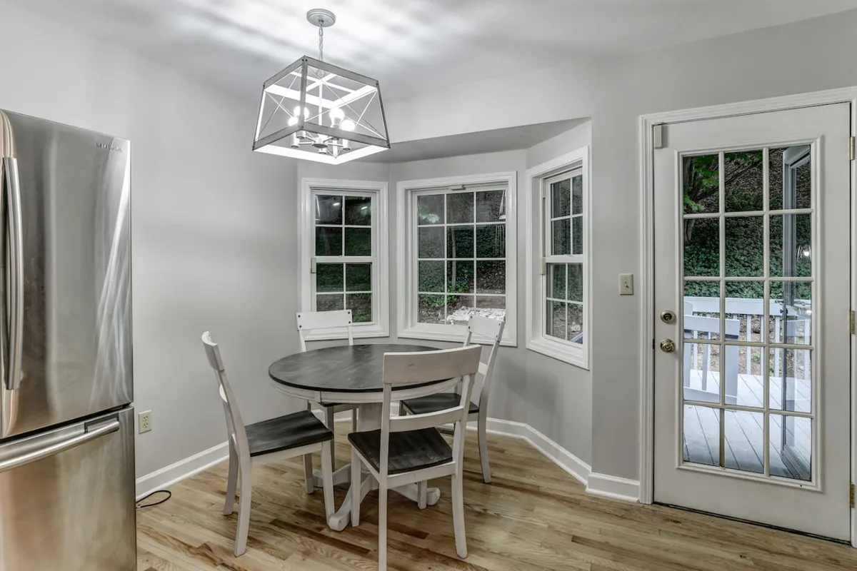 A warm, light-filled dining area with a round table and geometric light fixture, accented by large windows inviting natural light. The setting encourages group meals, games, and social interaction, reinforcing the home's capacity for memorable group experiences.