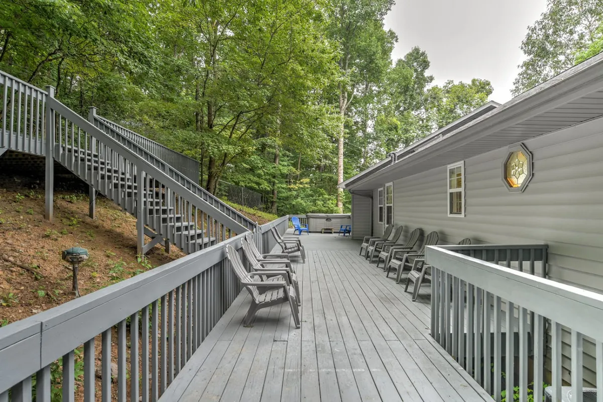 A spacious wooden deck with lounge chairs, a staircase, and mature trees nearby. The area is designed for both relaxation and social gatherings, offering views of the surrounding forest and a feeling of seclusion.