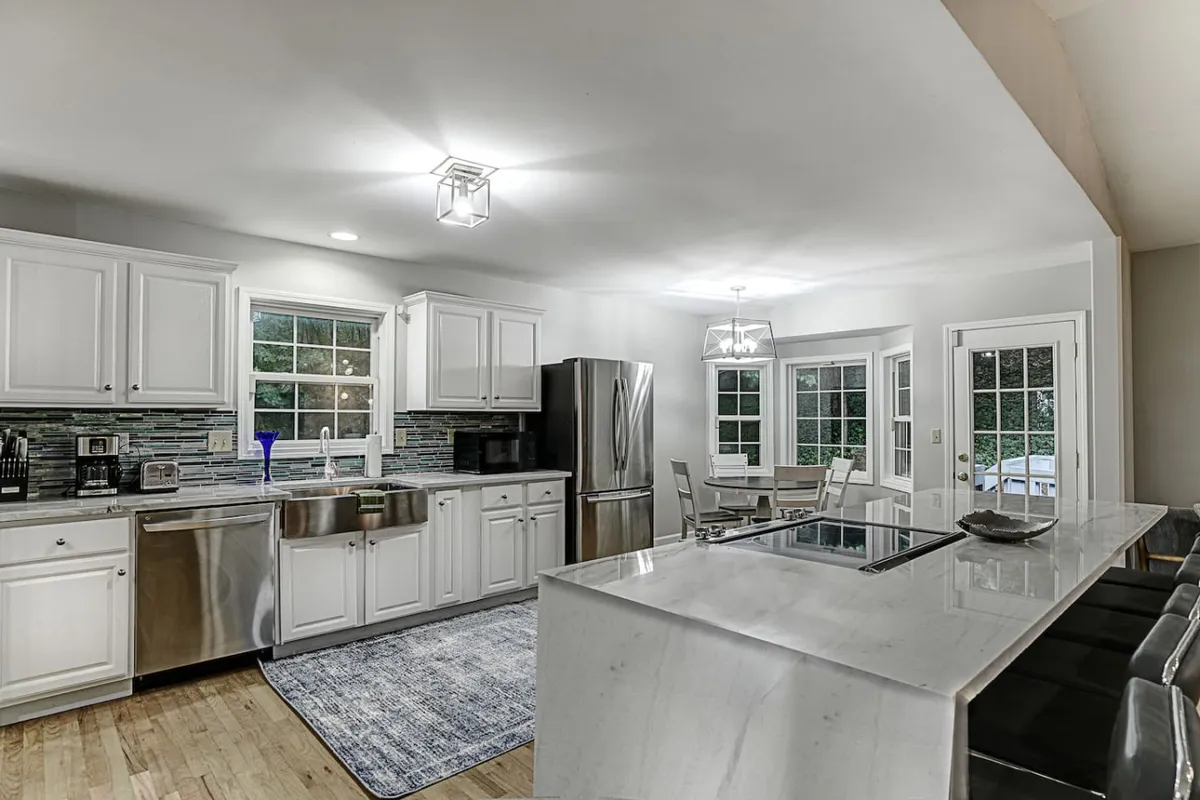 A spacious, sunlit kitchen with a large island, stainless steel appliances, and windows flooding the space with natural light. The open layout is designed for cooking, entertaining, and casual dining, with ample room for group activities.